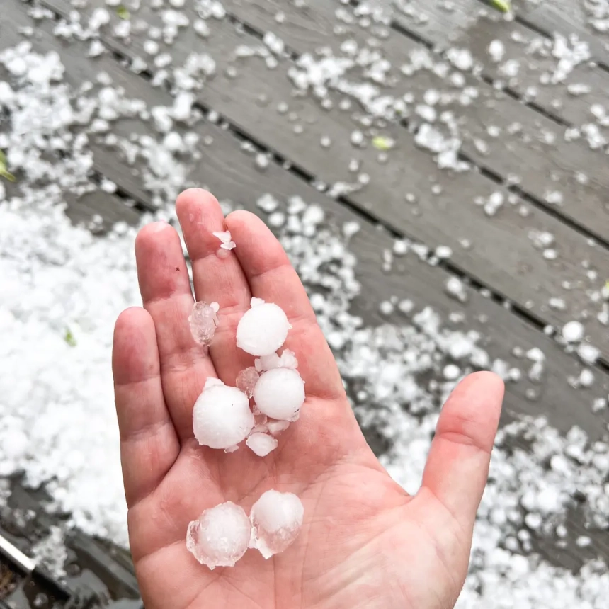 Large hailstone held on a damaged roof, emphasizing the impact of hail on roof replacement needs.