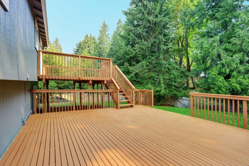 Rich-toned wood deck with Adirondack chairs overlooking a wooded lake, designed by custom wood deck builders.