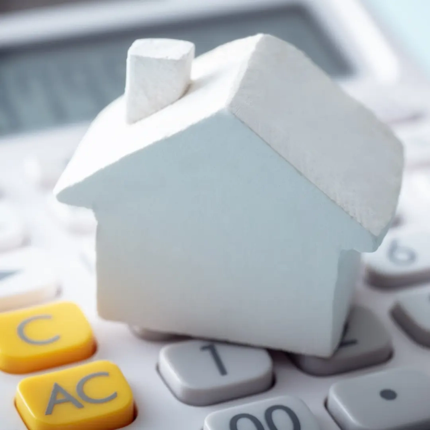 A white house model placed on a calculator representing local roofing companies that finance home improvement projects.