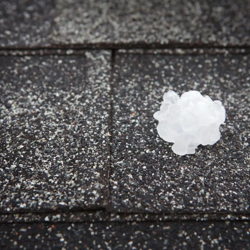 Large hailstone resting on asphalt shingles, illustrating the potential severity of hail damage roof replacement.