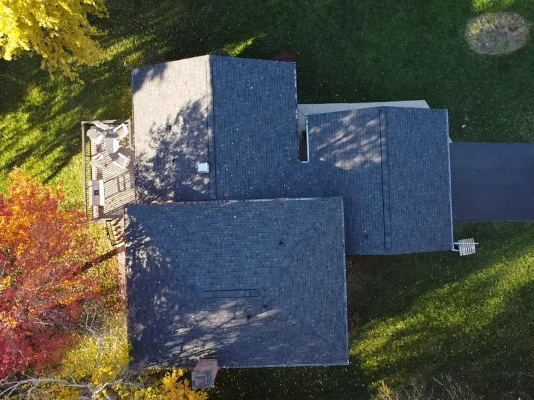 Aerial view of dark asphalt shingle roof on home surrounded by fall trees after roof repair in Wheaton IL