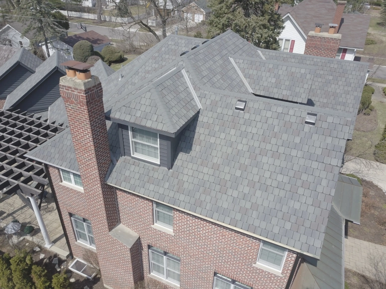 Drone view of new gray architectural shingle roof with chimney and dormers on brick home in Aurora IL